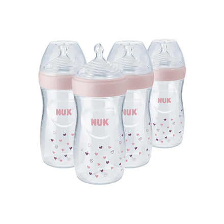 Four NUK baby bottles with pink caps and heart patterns on a white background