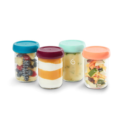 Four glass jars with colorful lids containing different types of food on a white background